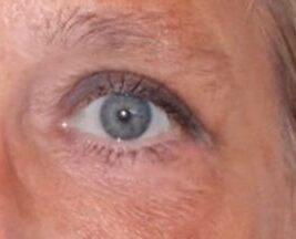 Nærbillede af et blågråt øje med tydelig sort eyeliner langs øjenkanten og let mascara på vipperne. Øjets iris viser nuancer af blå og grå, omgivet af hvide øjenområder. Den omkringliggende hud har naturlig struktur med fine linjer og let solbrun tone. Et velplejet øjenbryn kan ses øverst, og billedet fokuserer klart på øjets detaljer og makeuputtryk.