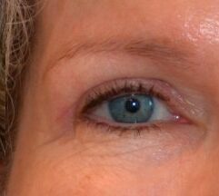 Nærbillede af et lystblåt/grønt øje med tydelig mørk pupil og let glans. Øjenfransene er definerede og synes let at være påført mascara. Brynet er tyndt og velplejet. Hud omkring øjet viser fine linjer og naturlig tekstur. Billedet fokuserer på øjets farve og detaljer med blødt lys, der fremhæver irisens nuancer og øjenvippenes kontur.