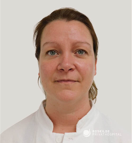 Forfra portræt af kvindelig patient iført clinicjakke med kort opsat hår og neutralt ansigtsudtryk mod lys baggrund. Billedet dokumenterer ansigt og hals og bruges af Roskilde Privathospital som før- eller efterbillede i forbindelse med ansigtsløft (ansigt), hos en klinik med 30 års erfaring.